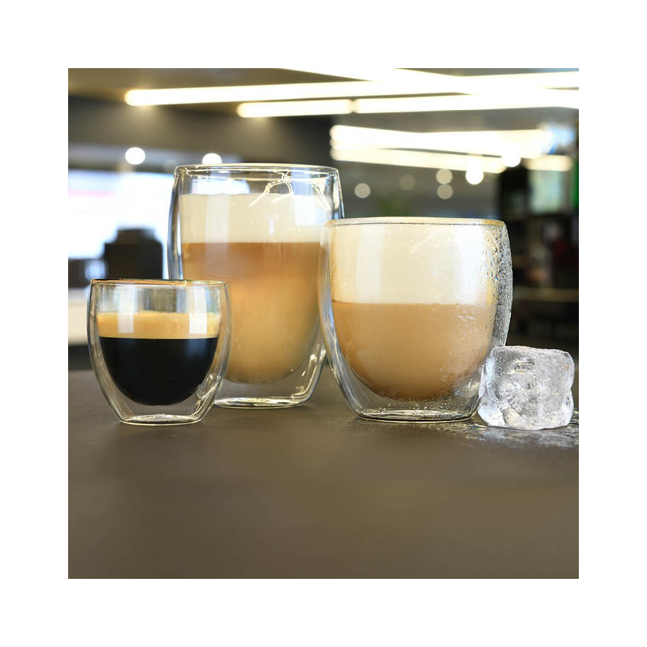 Three double-walled glass cups with different coffee drinks, alongside an ice cube, on a gray surface