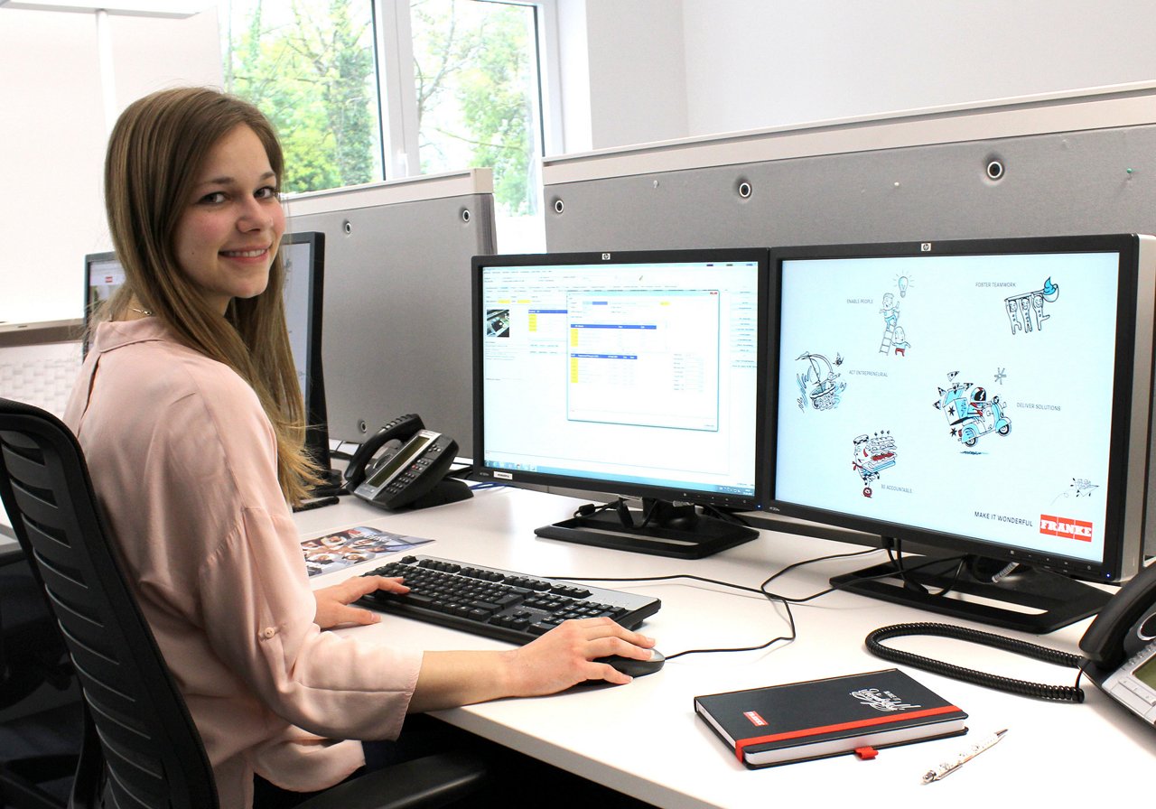 Woman sits and dual monitors and works on a customer report