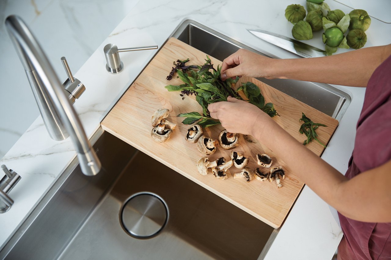 Vegetables being prepped over a Franke Professional stainless steel sink on an over-the-sink cutting board. 