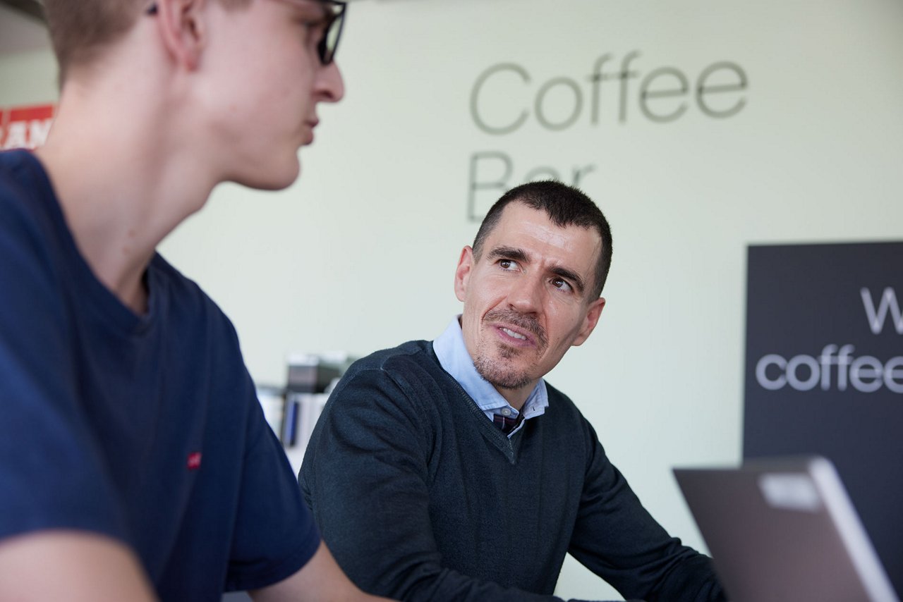 Two men seated at a table, engaged in conversation, with "Coffee Bar" text in the background