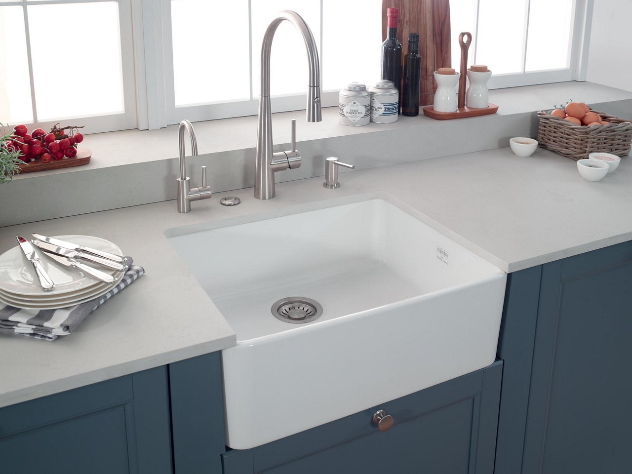 Farmhouse style kitchen with  blue cabinets, light countertops and a white apron front fireclay sink and stainless steel faucet 