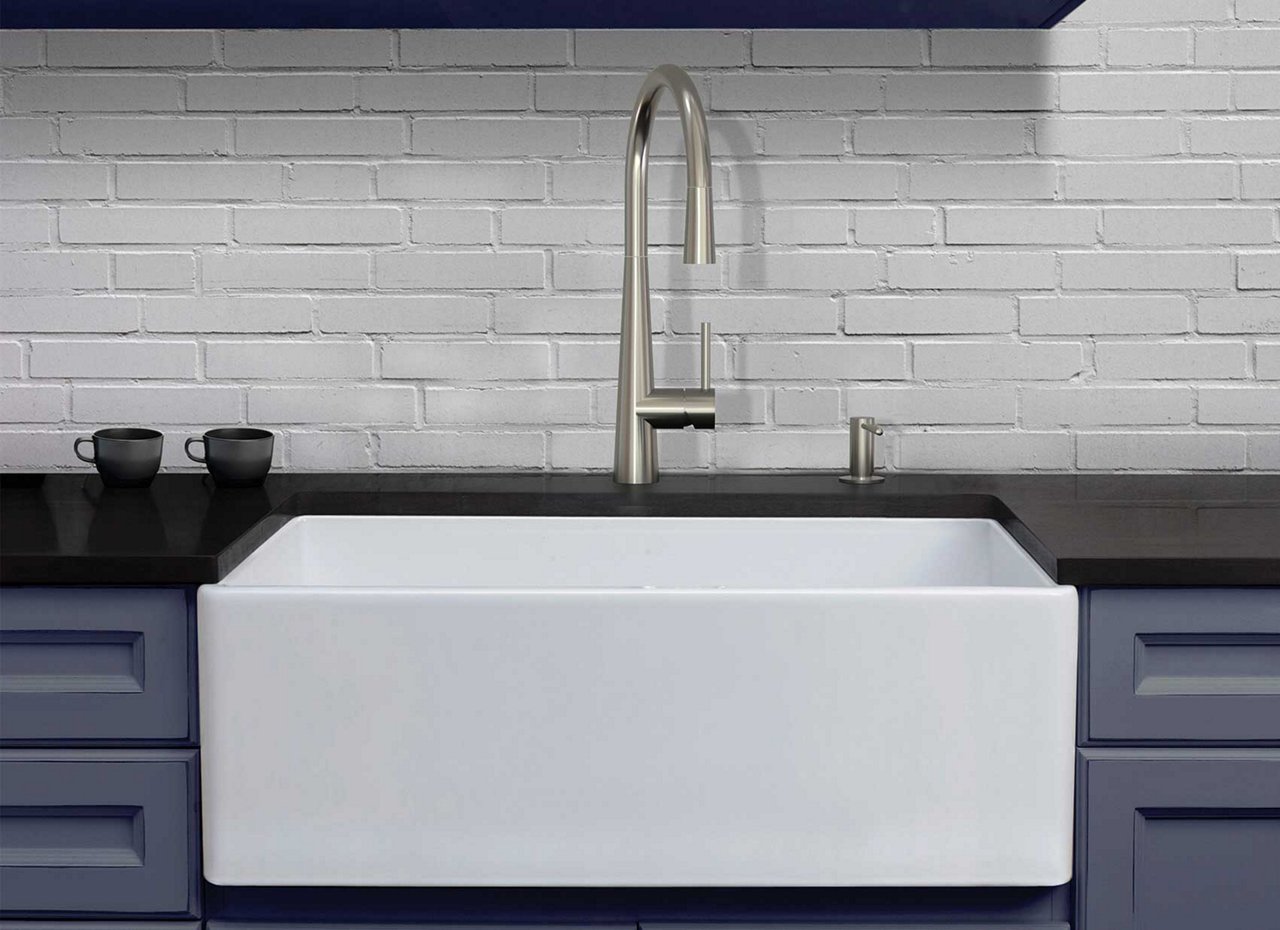 White apron front farmhouse sink in blue cabinets with a black countertop