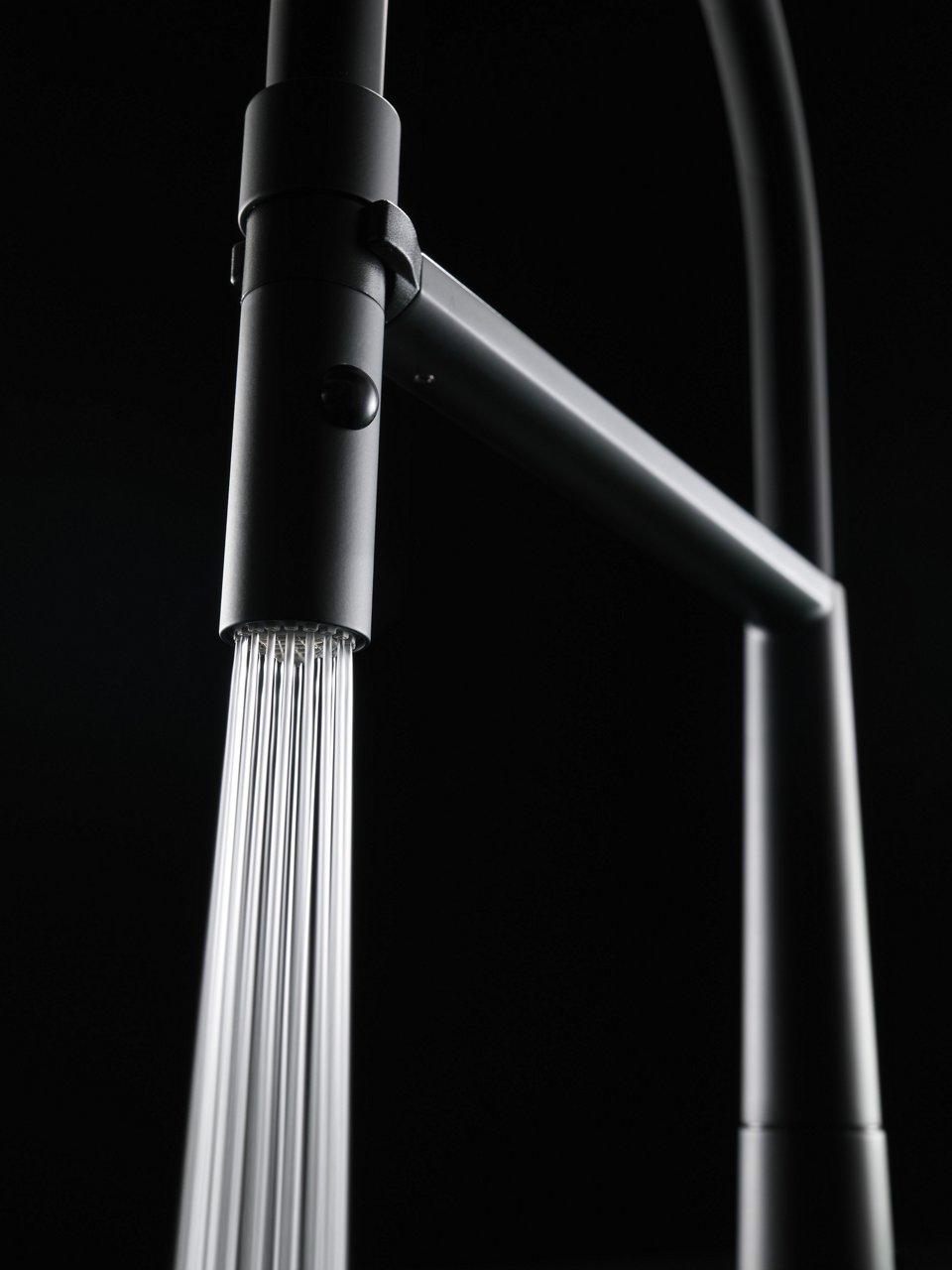 Zbliżenie na nowoczesną baterię kuchenną Franke w matowym, czarnym wykończeniu, z której płynie strumień wody. Tło utrzymane w ciemnej tonacji podkreśla elegancję produktu.