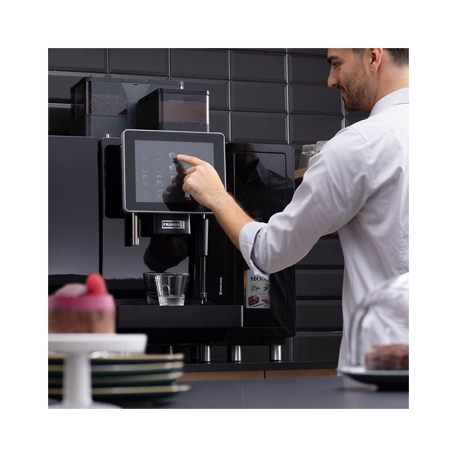 Franke Coffee Systems, man behind bakery shop counter, selecting beverage from fully automatic coffee machine Franke