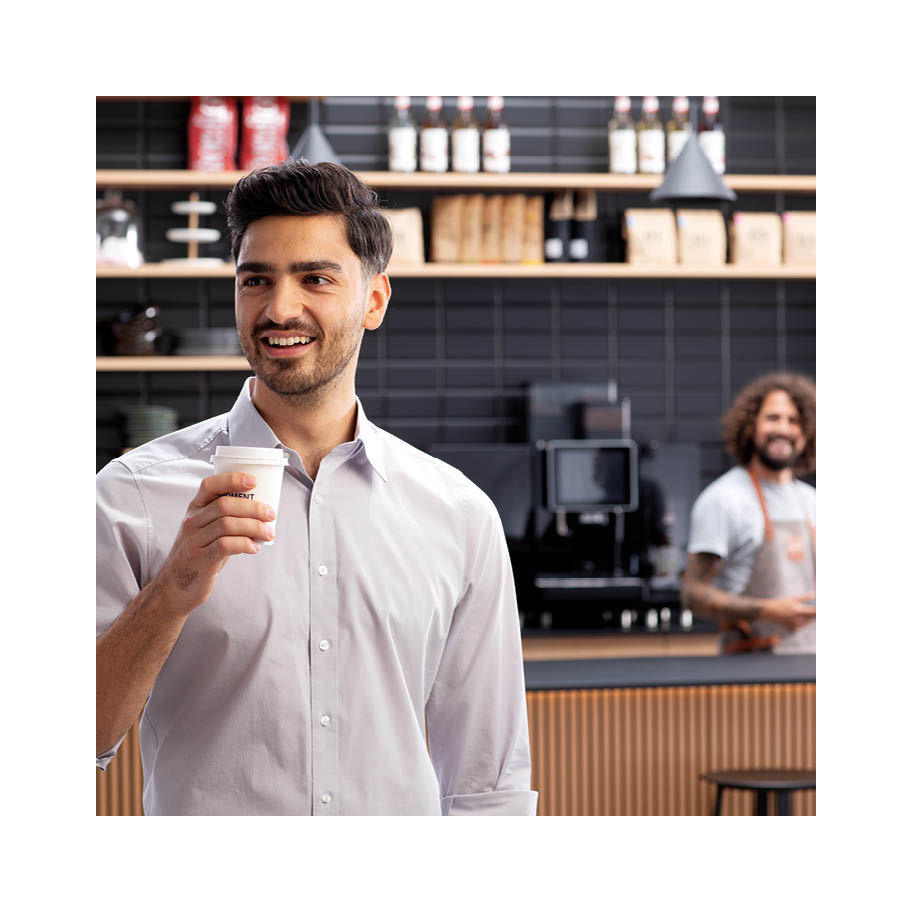 Franke Coffee Systems, man in coffee shop holding a coffee to go cup, counter and waiter near fully automatic coffee machine Franke in the background