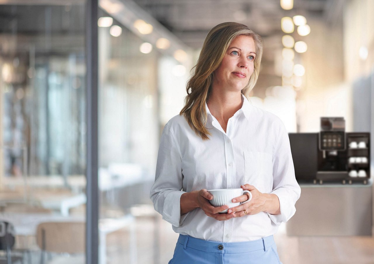 Franke Coffee Systems, woman holding a coffee cup in lobby, fully automatic coffee machine Franke in the background