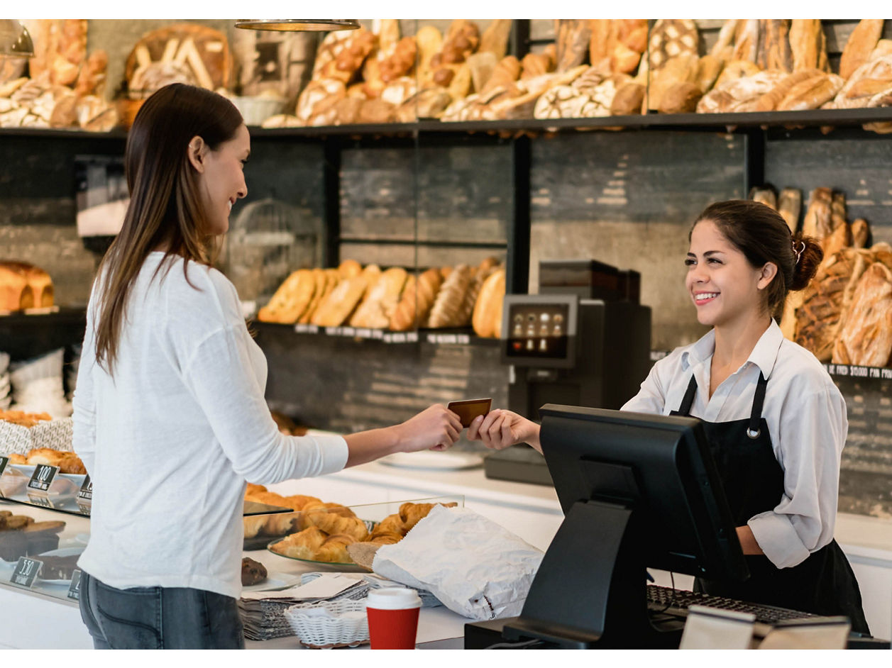 Franke Coffee Systems, woman buying bread in bakery store paying to woman shop assistant, fully automatic coffee machine Franke A300 in the background