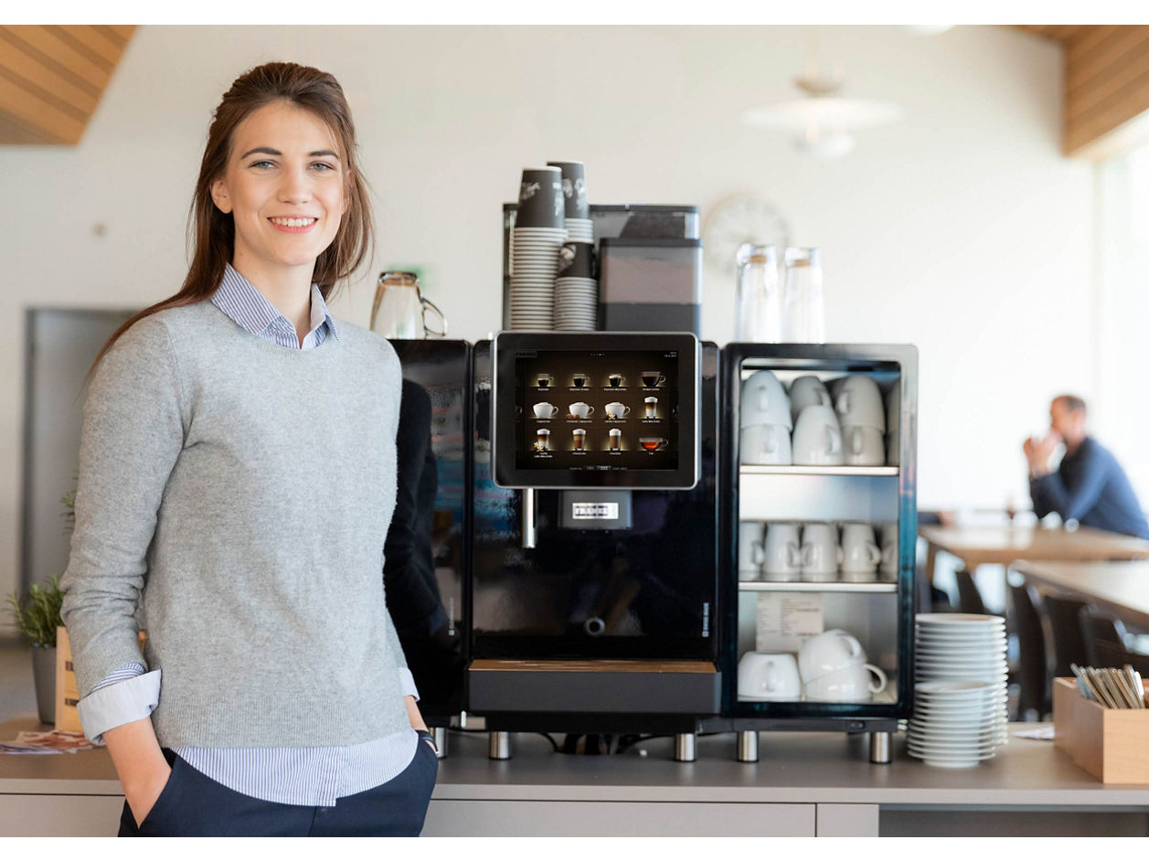Franke Coffee Systems, woman standing next to fully automatic coffee Machine Franke with cups, canteen environment