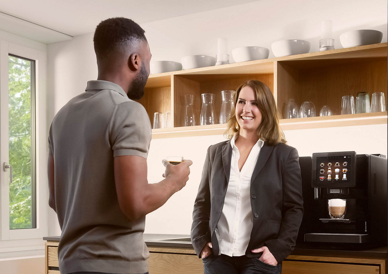 Franke Coffee Systems, man and woman having coffee break in the coffee corner of a workplace, fully automatic coffee machine Franke A300 in the background