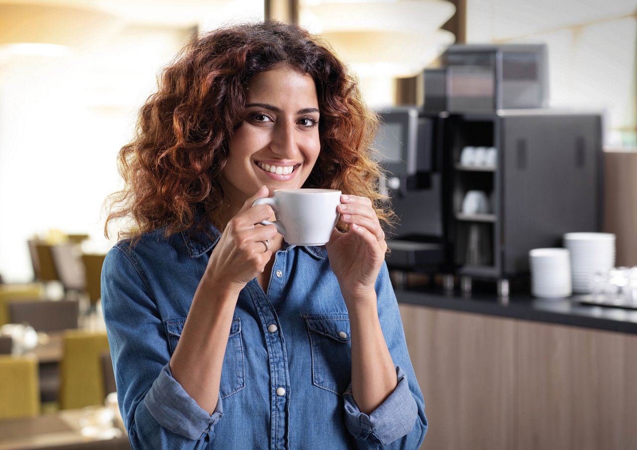 Franke Coffee Systems, woman drinking coffee, fully automatic coffee machine in the background