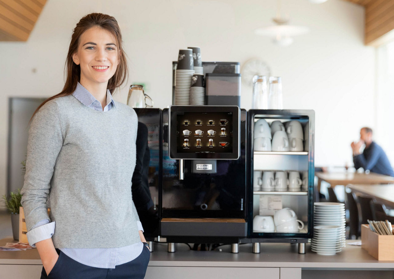 Franke Coffee Systems, woman standing next to fully automatic coffee Machine Franke with cups, canteen environment