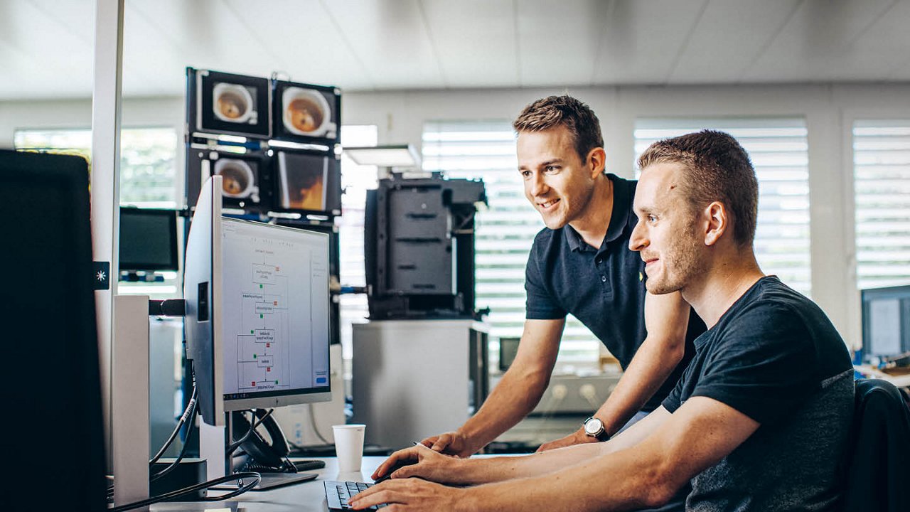 Franke Coffee Systems, coworkers infront of computer in the office, two men consulting, screens in the background