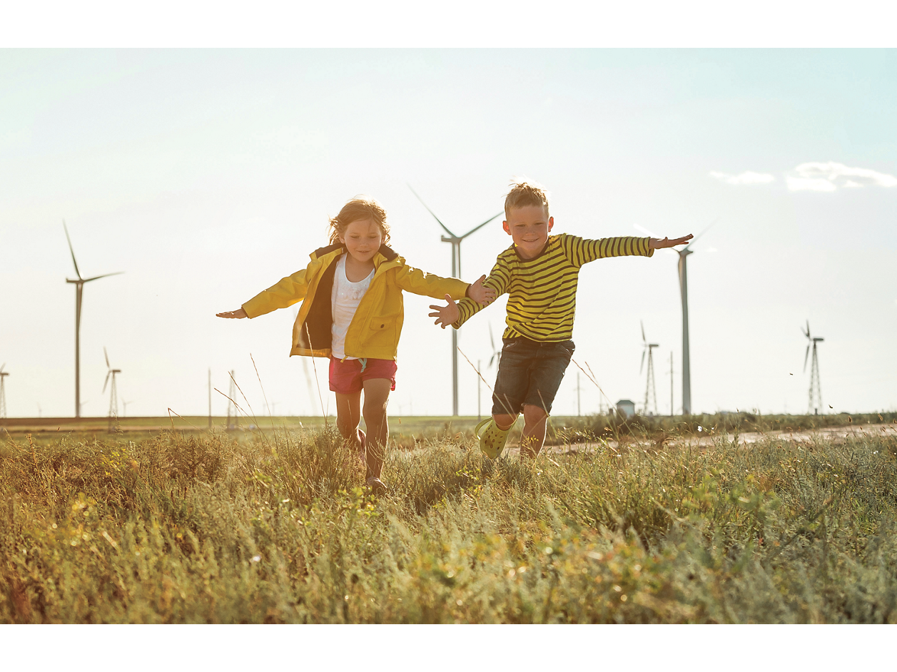 Two kids running on field in front of windmills