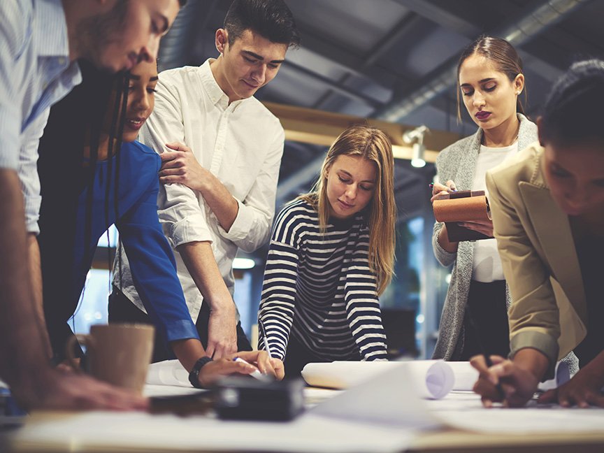 group of six young people standing around a table working