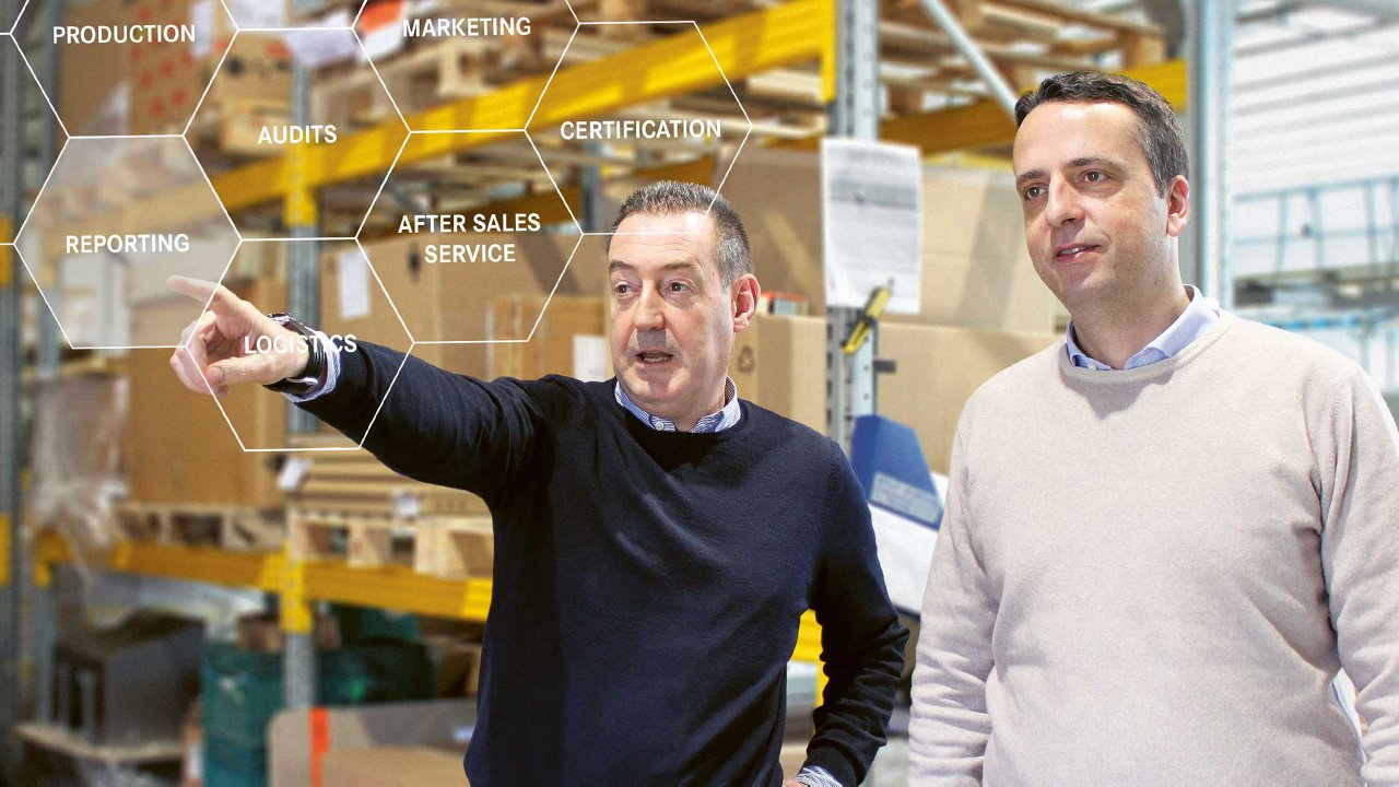 Two men in a warehouse observe something. One points ahead, while the other looks in the same direction. Overlay text includes terms like AUDITS and MARKETING. Shelves and industrial equipment are visible in the background