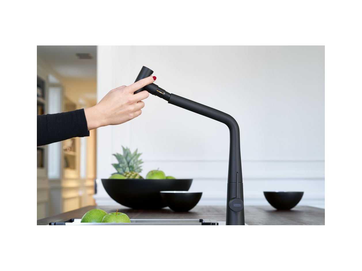 Nowoczesna bateria kuchenna Franke z czarnym, matowym wykończeniem i wyciąganą wylewką, w tle owoce na drewnianym blacie w jasnej kuchni.