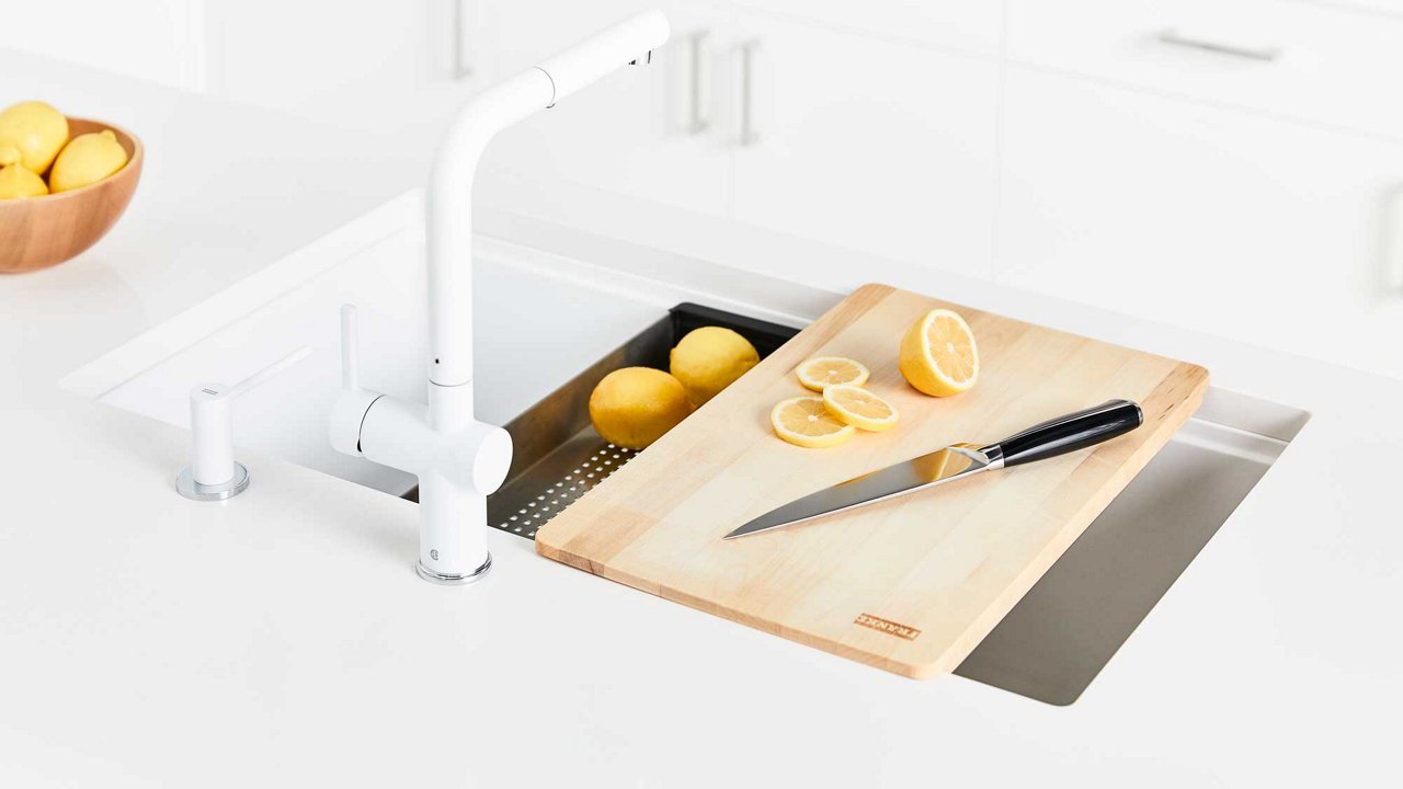 Lemons being sliced on a cutting board over a while kitchen sink