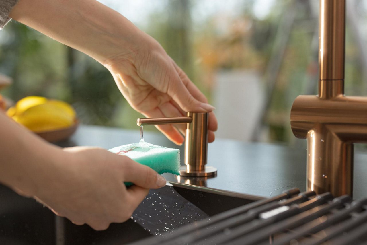 Person using a kitchen soap dispenser in copper finish