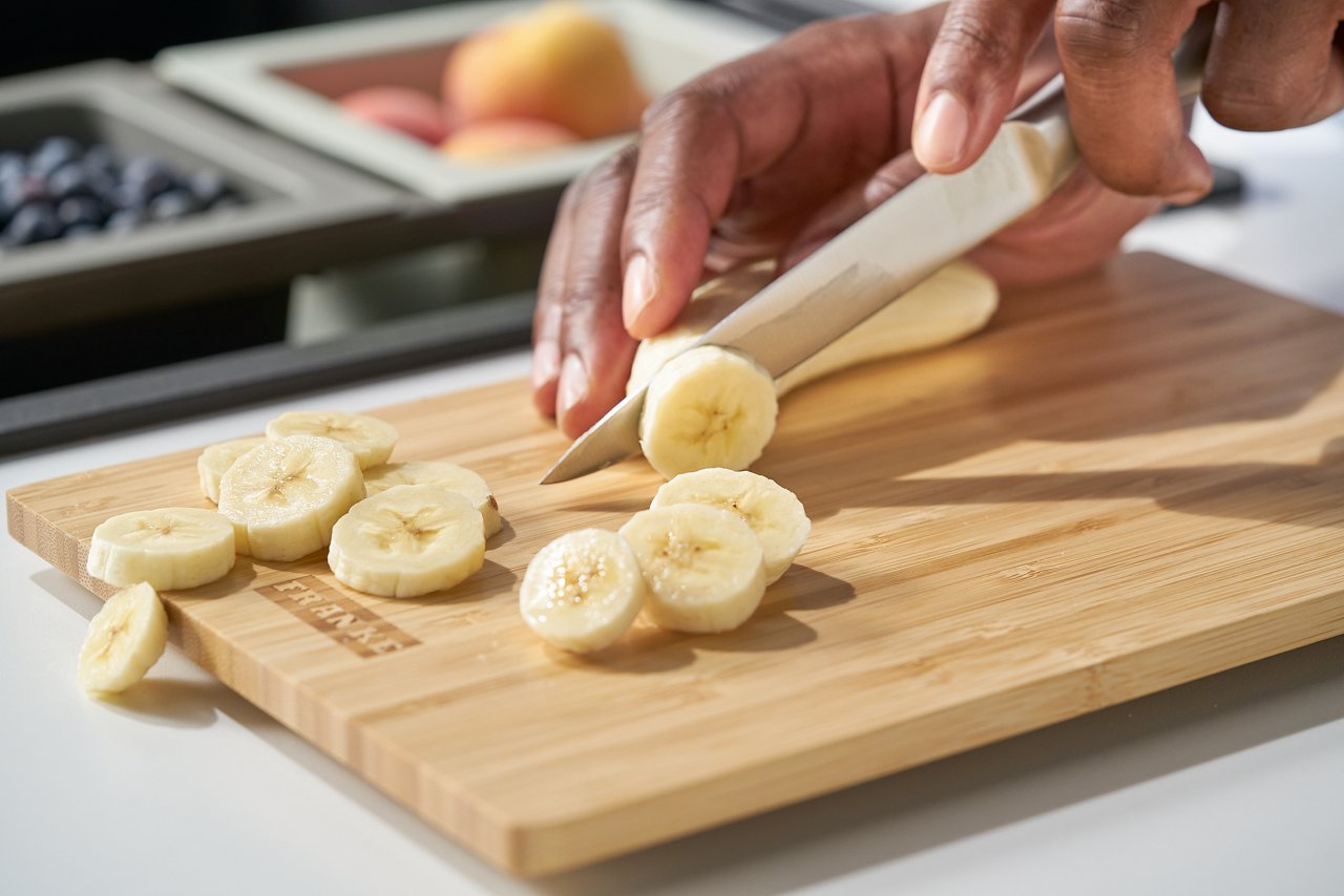 Snijplank waarop een banaan in schijfjes gesneden wordt