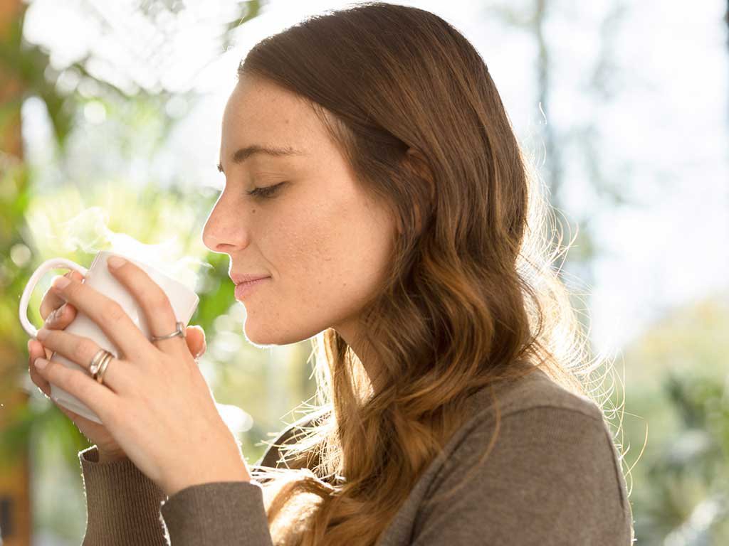 Woman with brown hair enjoying the aroma of her coffee 