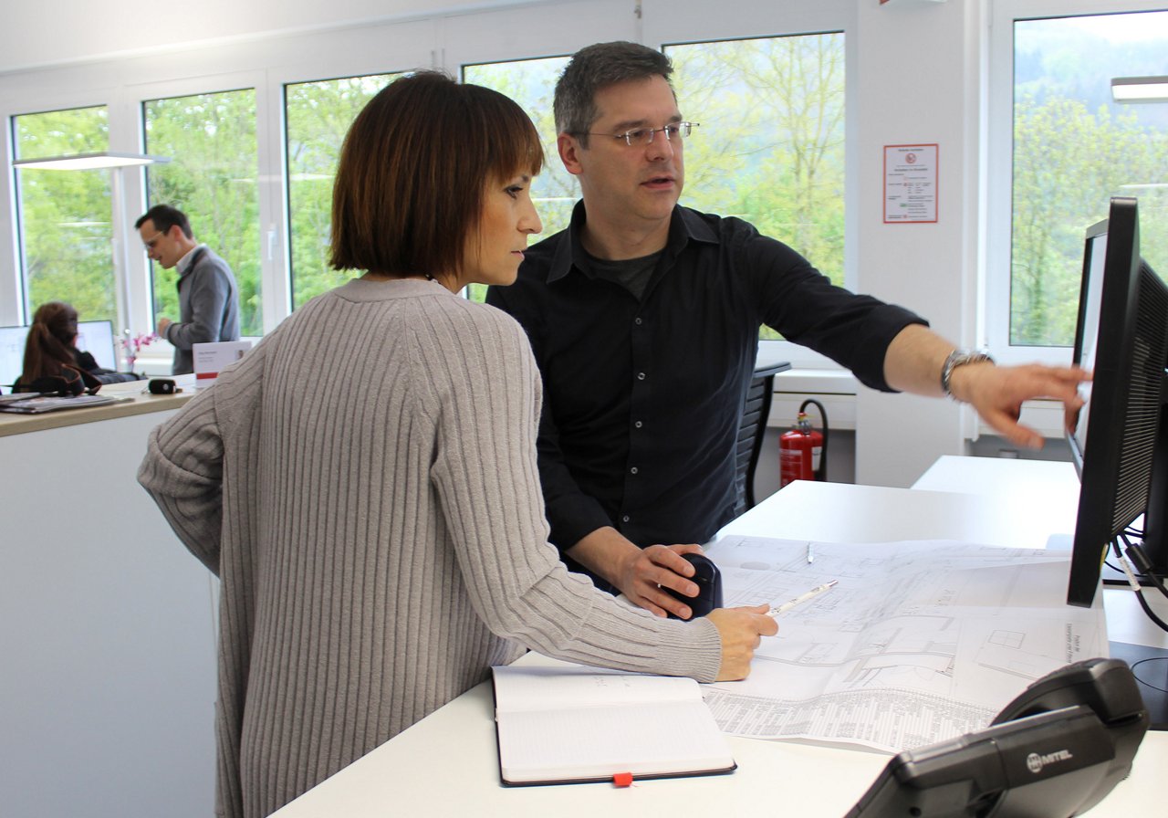 Program manager and customer work together, inspecing drawings at a workstation