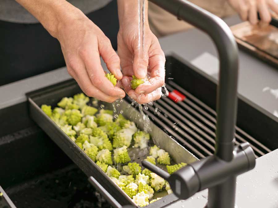 kitchen sink colander with vegetables being rinced.