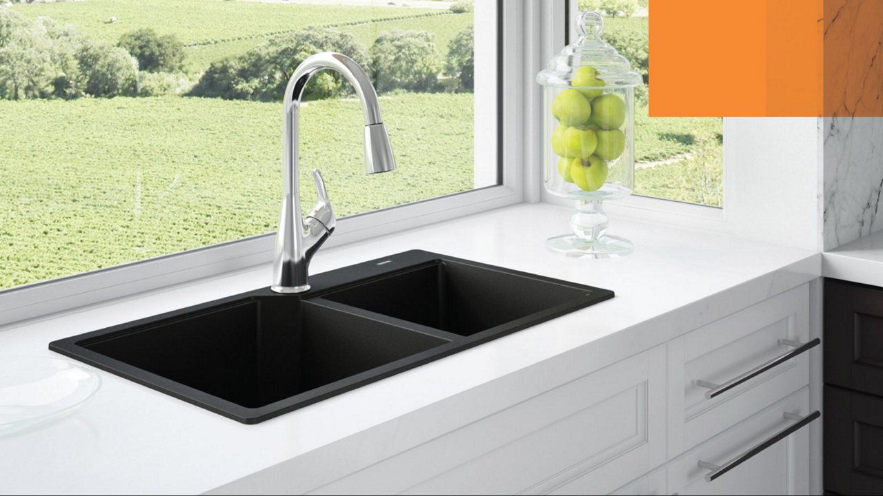 Kindred matte black double bowl granite kitchen sink with a chrome faucet in a white kitchen with a large window. 