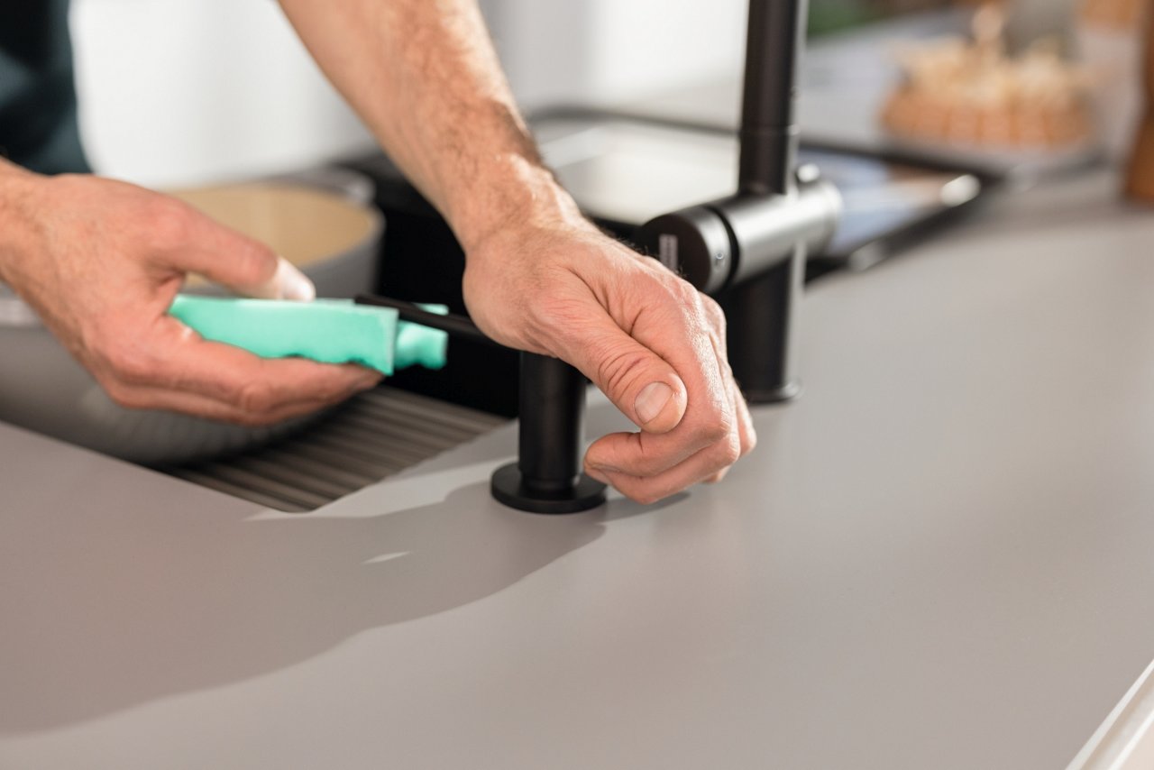 Gąbka nabiarająca płyn z czarnego dozownika Franke. Dozownik zamontowany na eleganckim, szarym blacie kuchennym, w tle rozmyte elementy stylowej kuchni.”