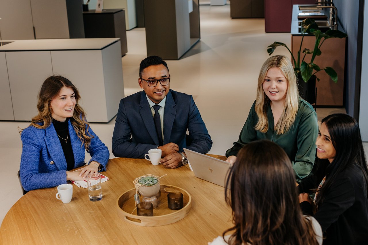 five people in an office setting engaged in conversation around a table