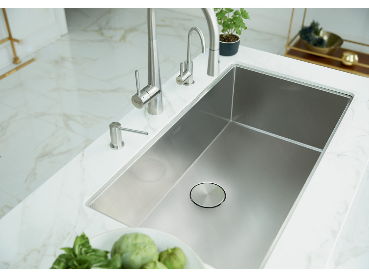 Modern Franke stainless steel kitchen sink with a stainless steel faucets set in a white marble countertop, featuring a view is into the sink showing the sleek round drain cover. 
