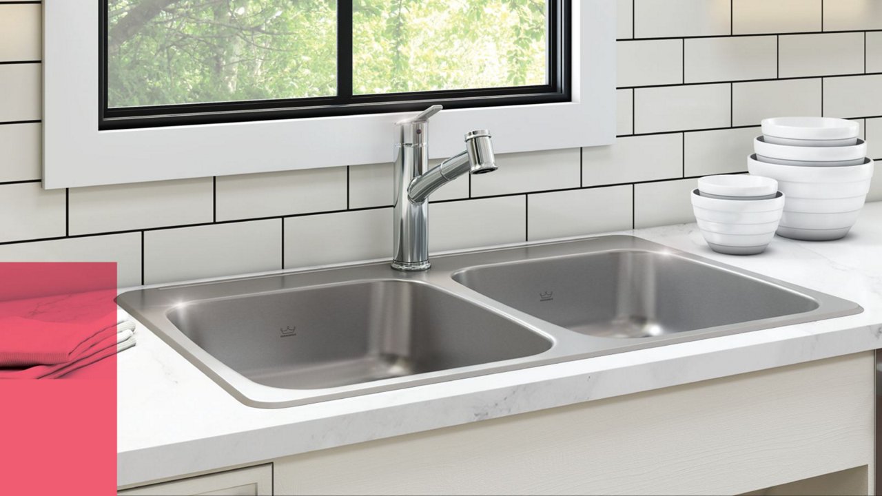 Close up of a Kindred ADA double bowl stainless steel kitchen sink and chrome pull out faucet  in a bright white modern kitchen 