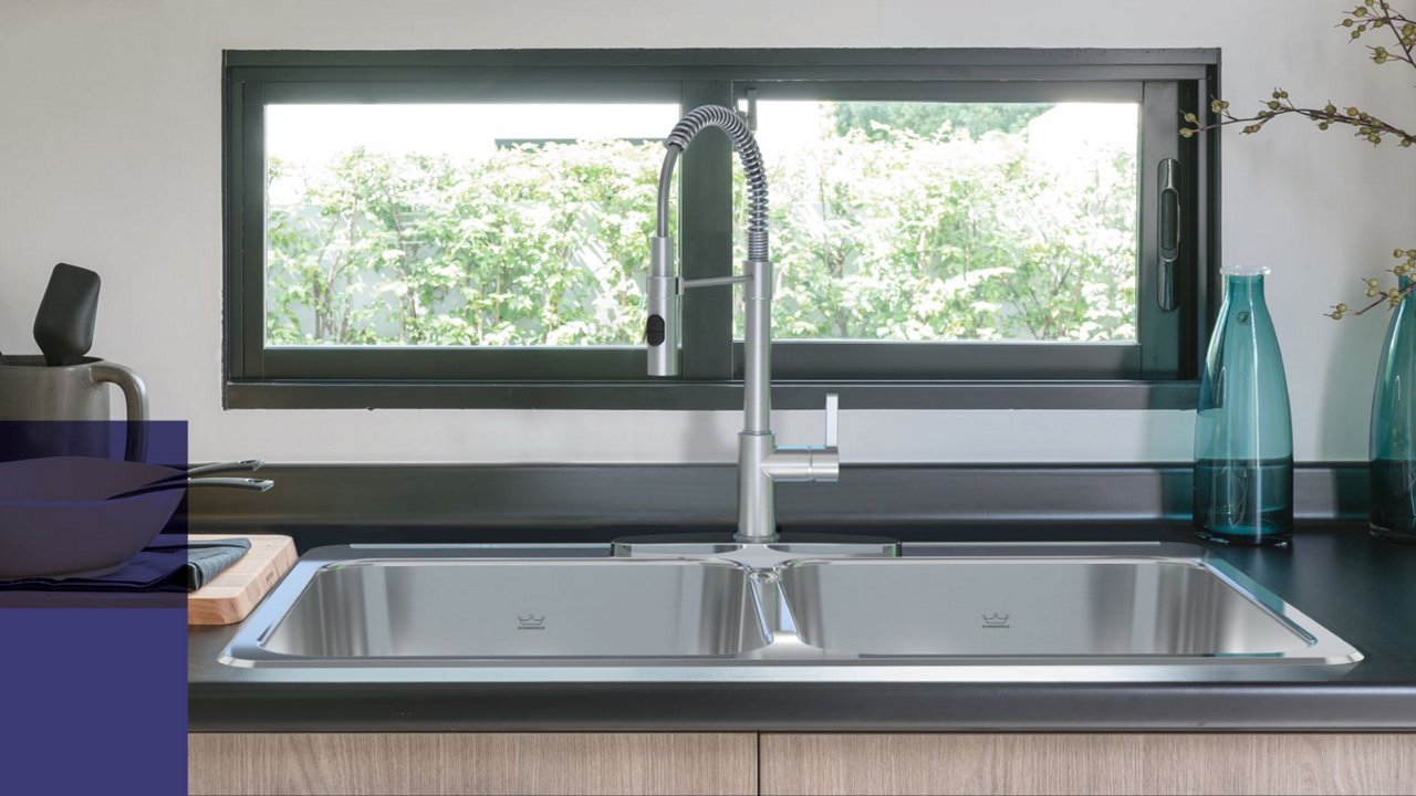 Close up of a double bowl stainless steel drop in kitchen sink and chrome faucet in a kitchen setting