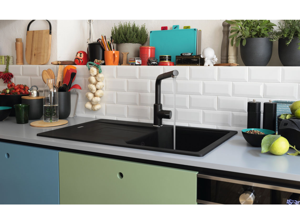 Widok z góry na nowoczesny, czarny zlewozmywak Franke o prostokątnym kształcie i gładkich krawędziach, z centralnym odpływem i srebrną baterią zamontowaną na górnej krawędzi. Zlewozmywak osadzony w jasnym blacie kuchennym, z subtelnymi akcentami żółtych elementów w rogach kadru.